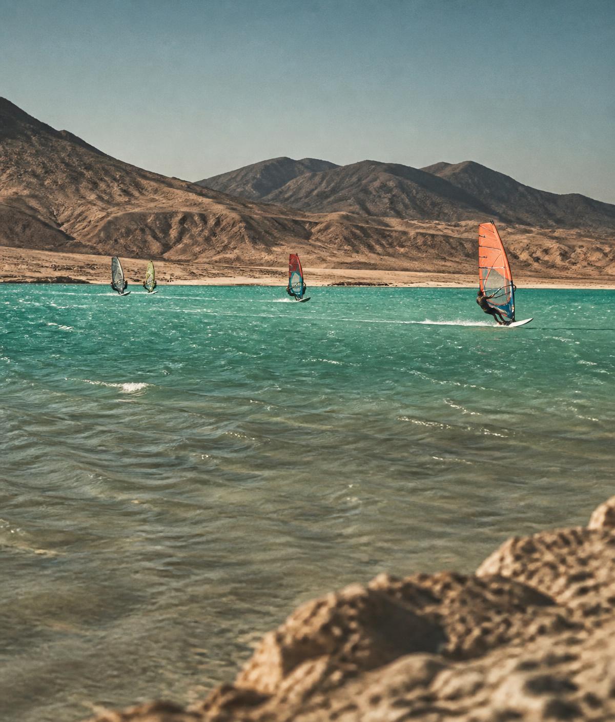 Laguna turquesa con velas de windsurf y costa árida bajo la luz de la tarde